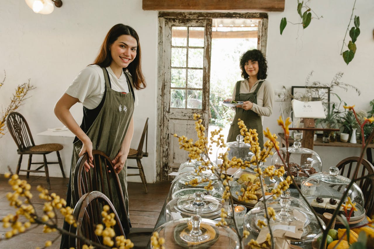 Two women in a cozy café setting preparing and serving delicious pastries with a cheerful demeanor.