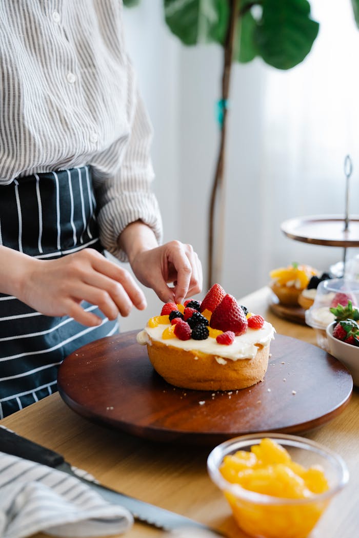 Chef decorates a cream-covered cake with fresh berries in a cozy kitchen setting.